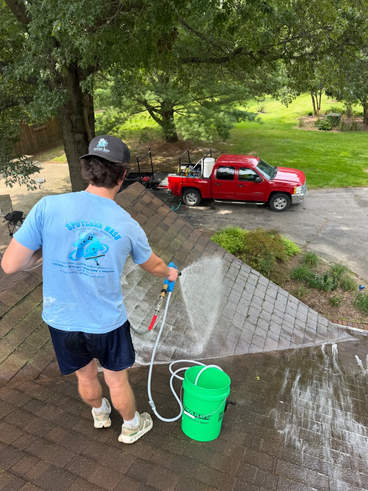 Spotless Wash technician applying a softwash treatment to a shingle roof