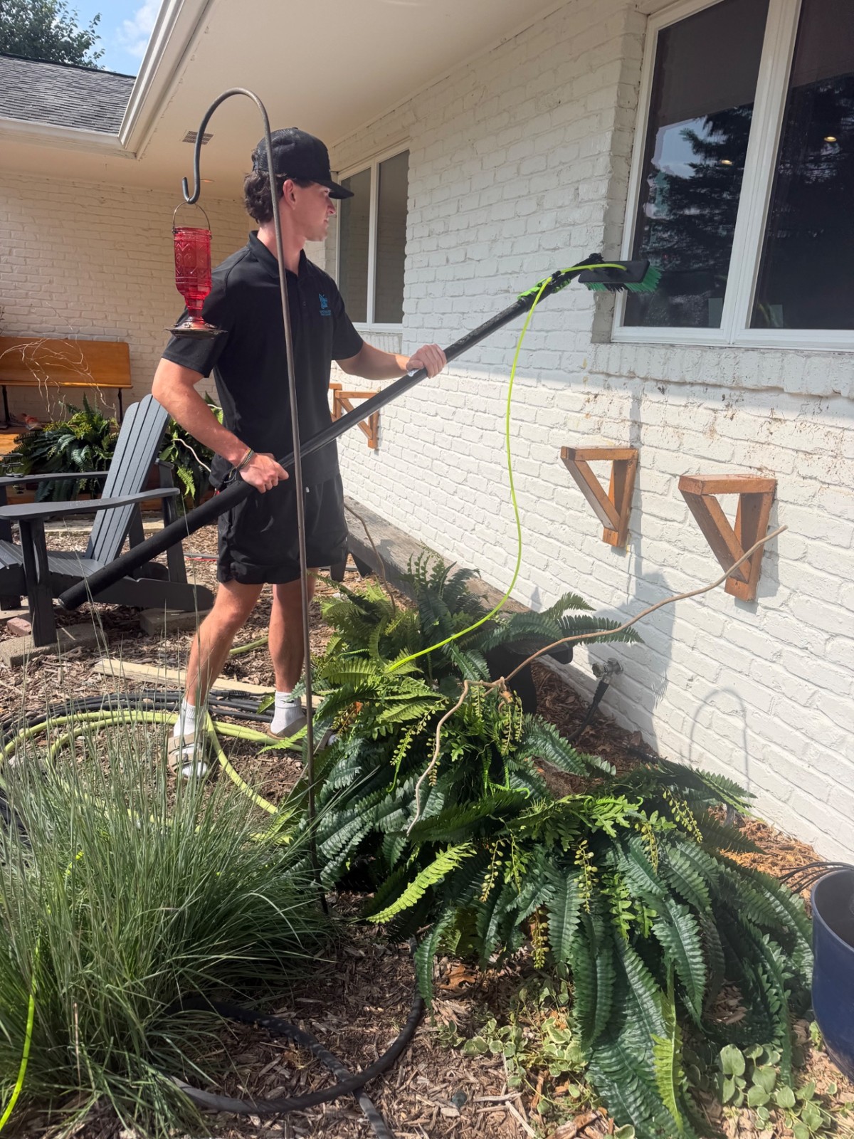 Spotless Wash technician cleaning exterior windows on a white brick home