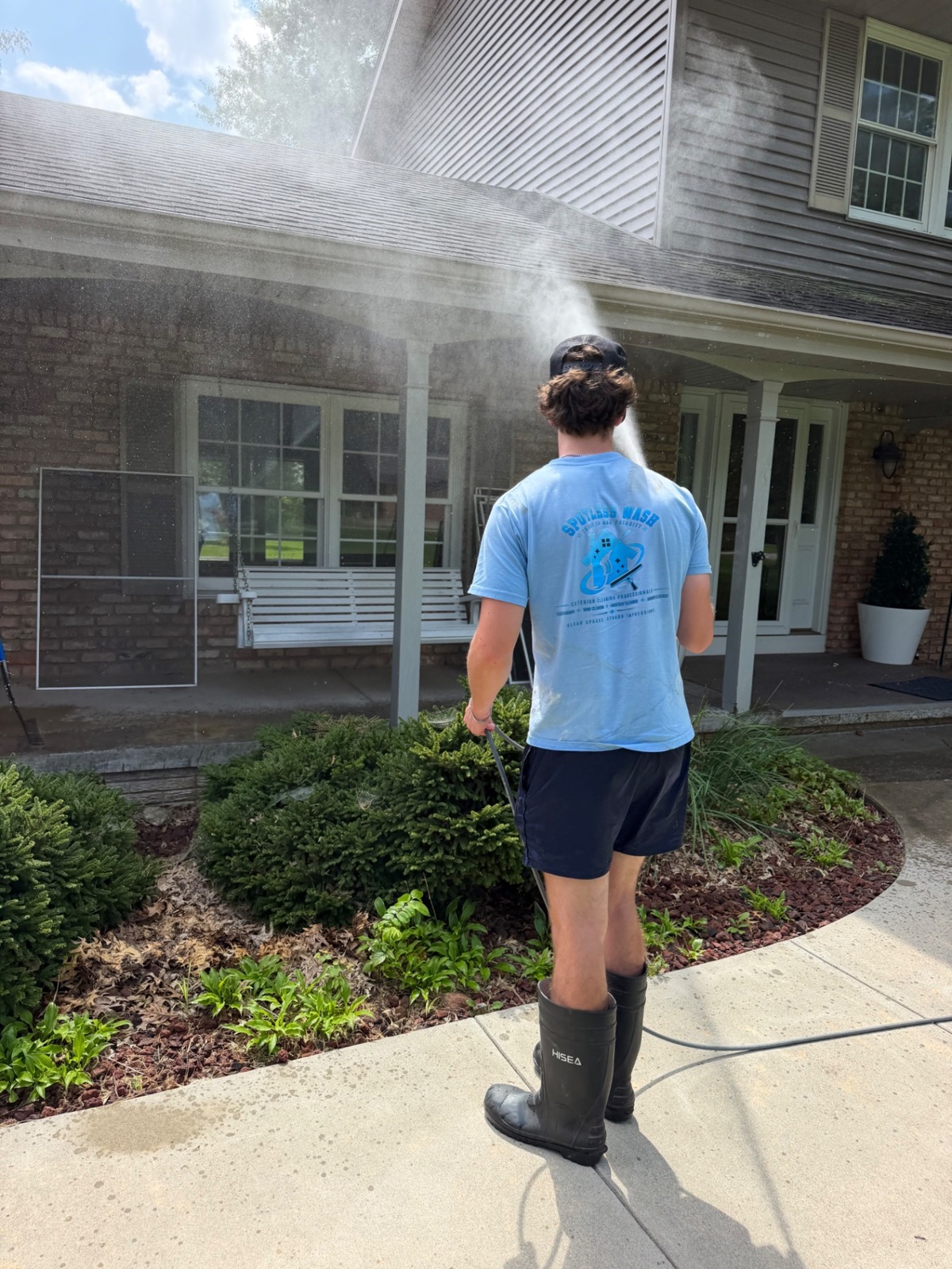 Spotless Wash technician washing a house exterior and front porch