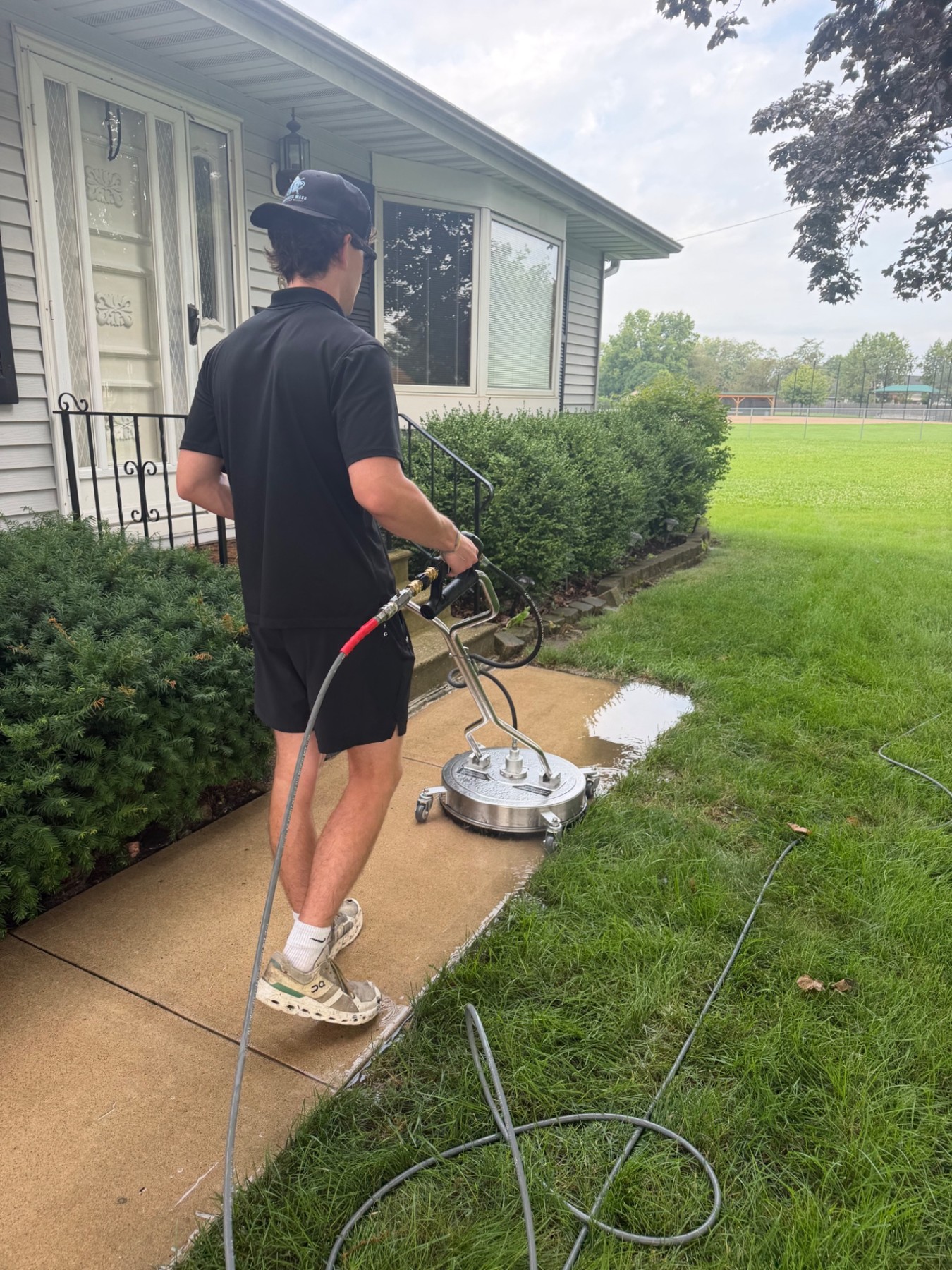 Spotless Wash technician using a surface cleaner on a concrete front walkway