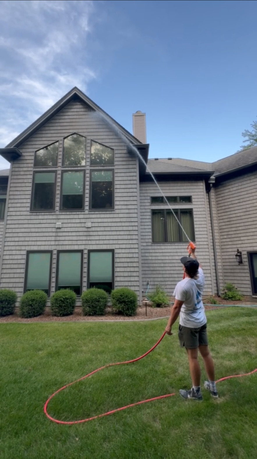 Spotless Wash technician soft washing the siding of a two-story home