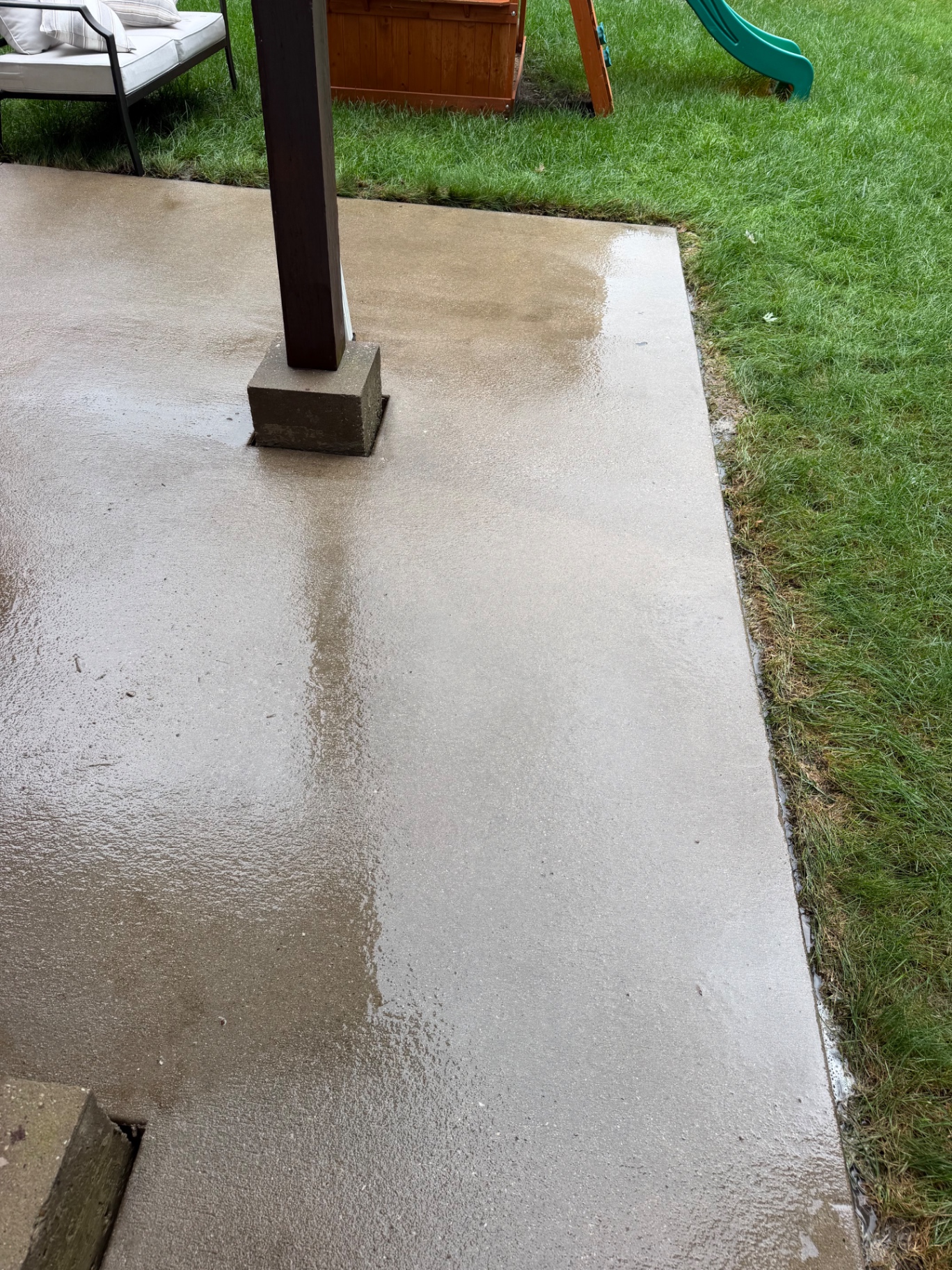 Freshly washed concrete patio beside a lawn and deck support